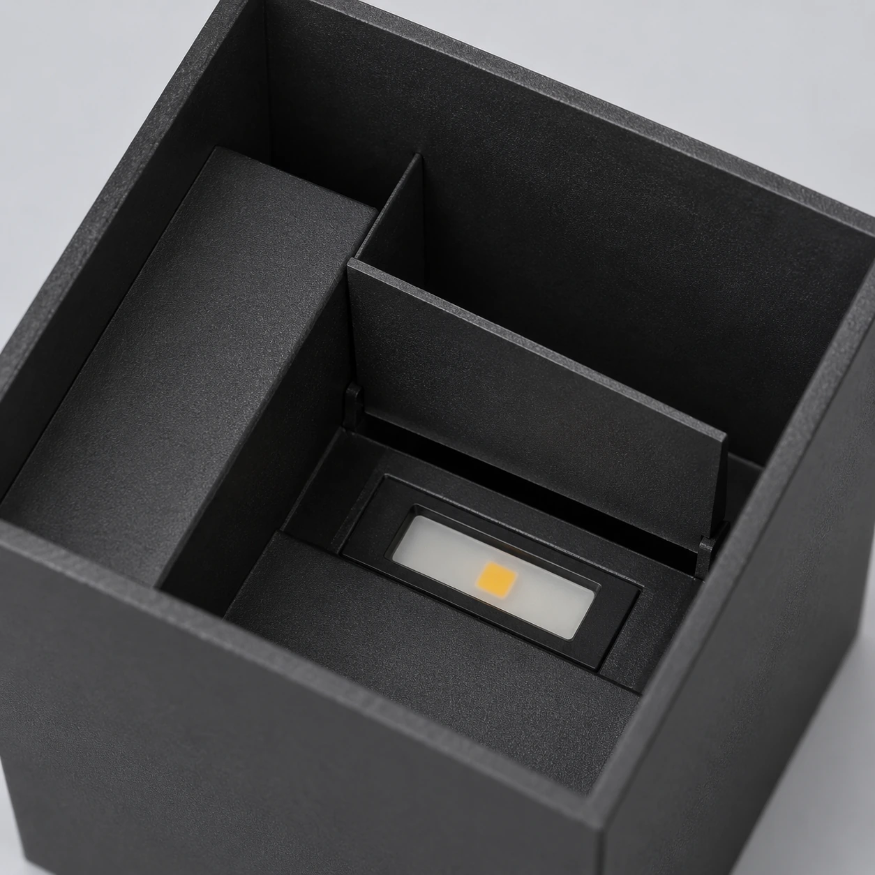 Le volet ouvert du cube noir découvre la barrette LED et sa pastille dorée au fond de la cavité
