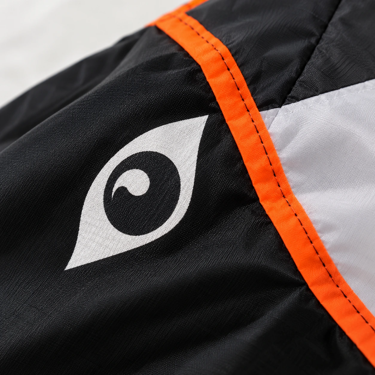 Gros plan sur l'oeil imprimé du cerf-volant baleine et sur la couture orange qui borde la voile noire