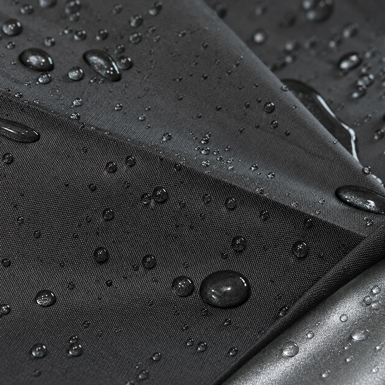 Gouttes de pluie perlant sur la toile noire, enduit argenté visible au pli