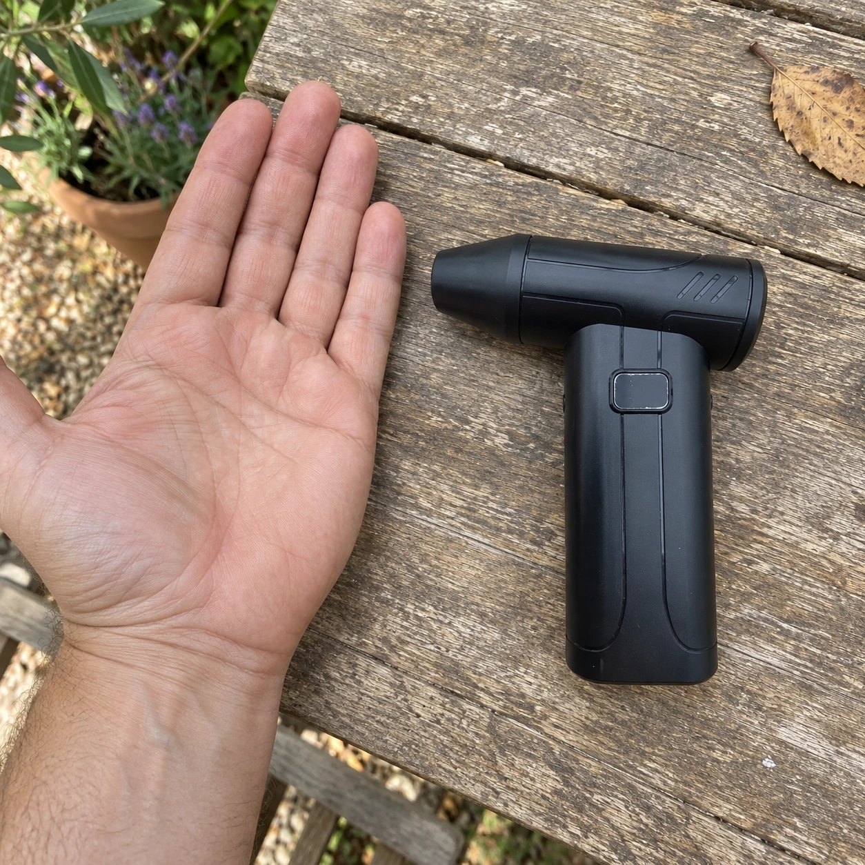 Mini souffleur rechargeable posé à plat, sa taille comparée à une main ouverte